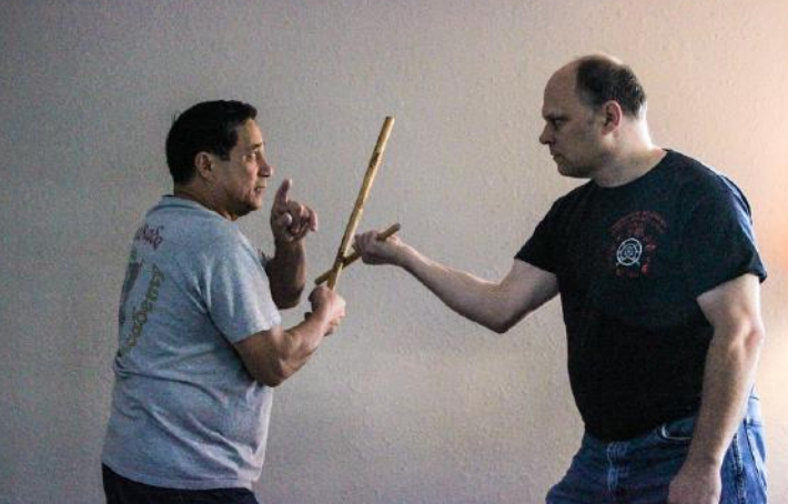 Two men are holding sticks and one is pointing at the other