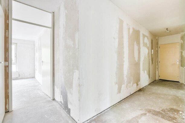 Hallway under construction; white walls with exposed patching, open doorways, concrete floor.