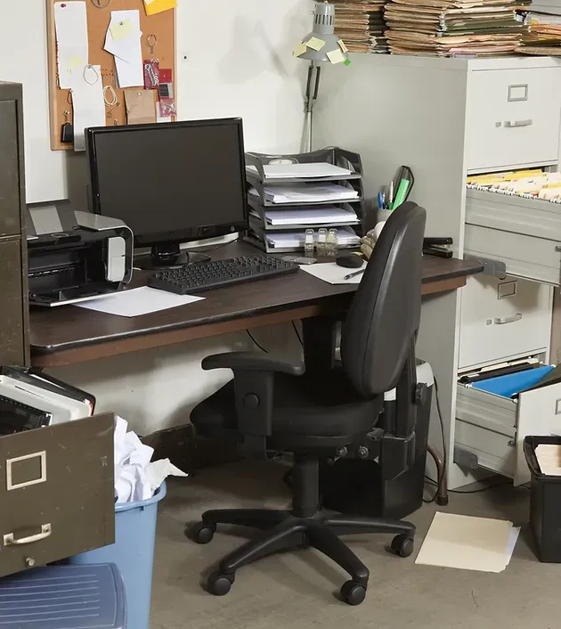 Cluttered office desk with computer, printer, filing cabinets, and office chair.