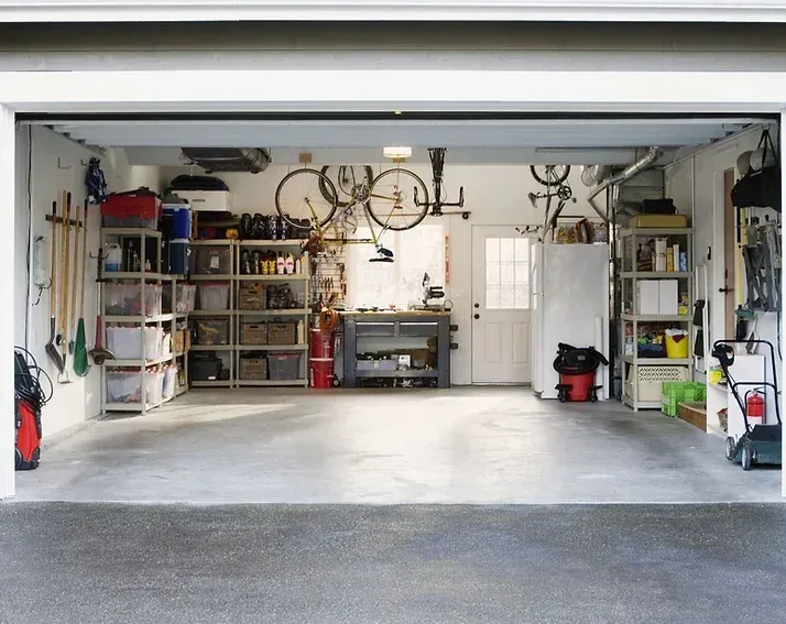 Garage interior, open door. Bicycles, tools, and storage shelves filled with items are visible.