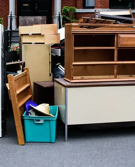 Pile of discarded furniture on a city street: refrigerator, shelves, desk, and a blue bin.