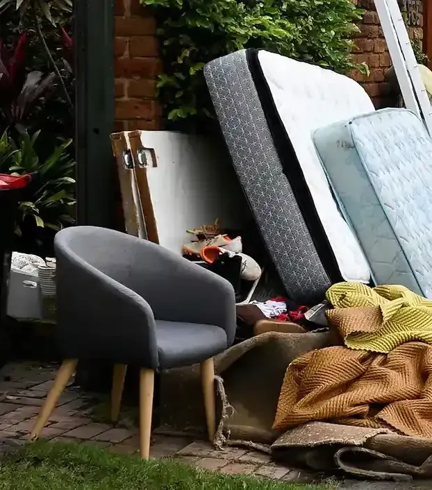 Gray chair sits near pile of discarded mattresses, furniture, and other debris outside a building.