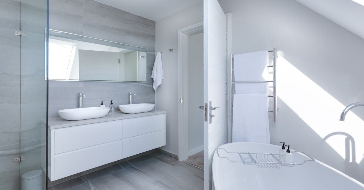 Modern white bathroom with dual sinks, tub, and towel warmer; bright, airy space.