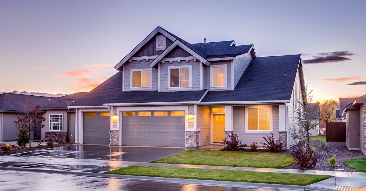 Two-story gray house with a dark roof at dusk. Three-car garage, green grass, and a clear sky.