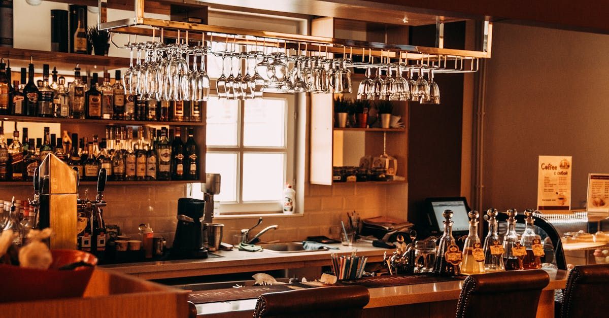 Interior view of a bar with bottles of alcohol, hanging glasses, and a window.