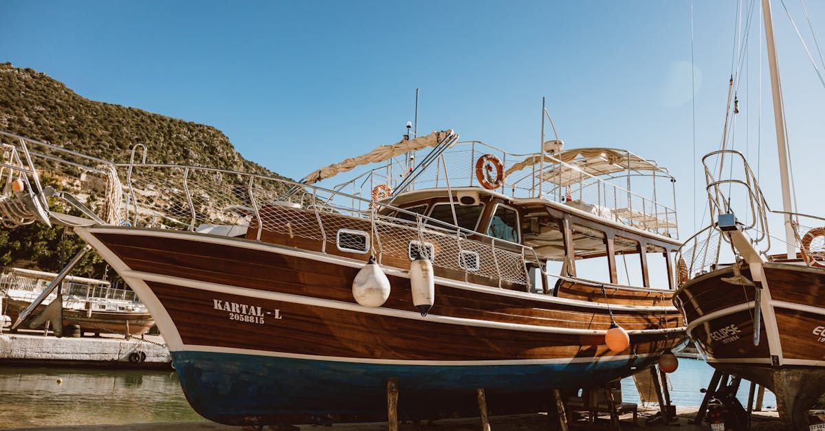 Wooden boat docked in harbor, blue hull, brown wood, sunny day, mountains in background.