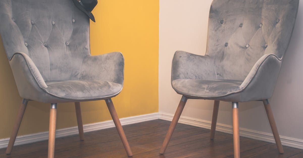 Two gray upholstered armchairs against yellow and white walls, a hat on one chair.
