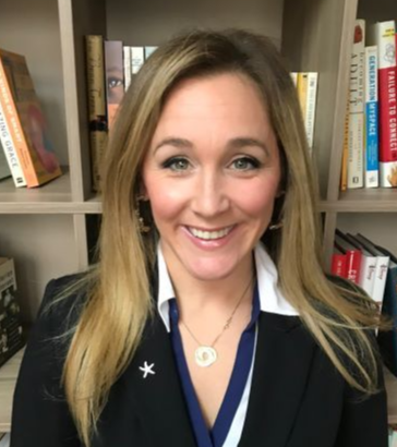 Smiling woman in a black blazer and white shirt standing in front of bookshelves