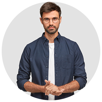 Man in glasses and blue shirt, hands clasped, stands in front of a white background.