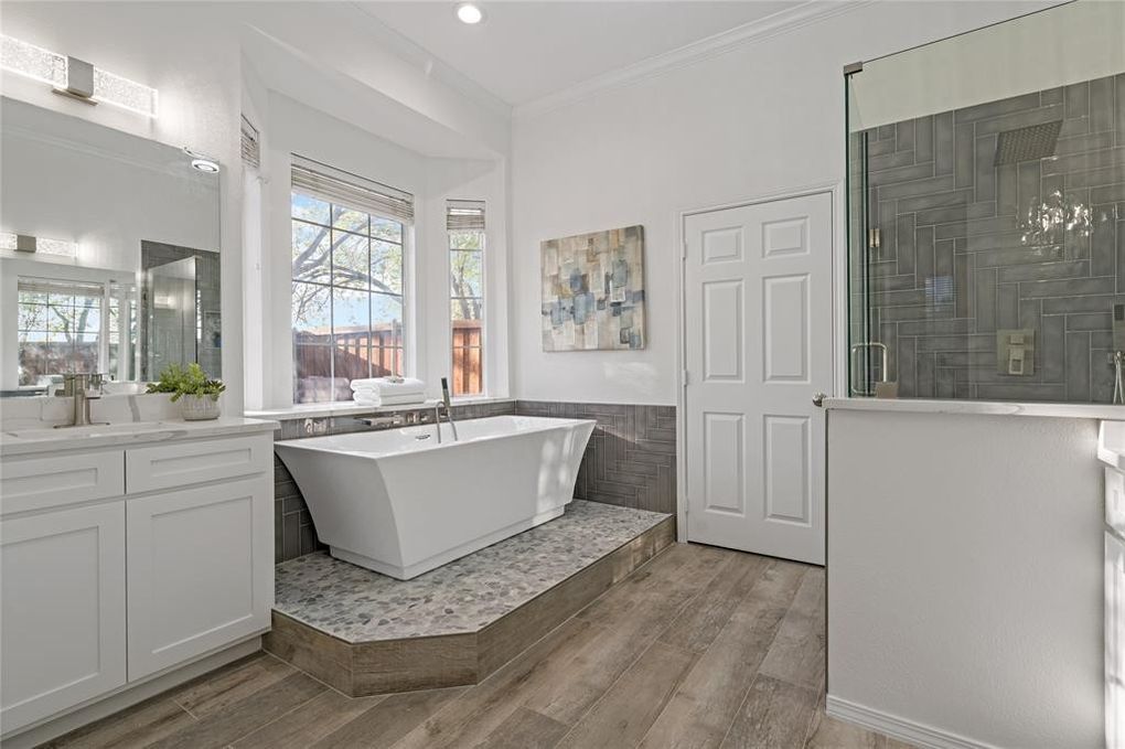Couple in white outfits looking out a window near their suitcase in a bright room.