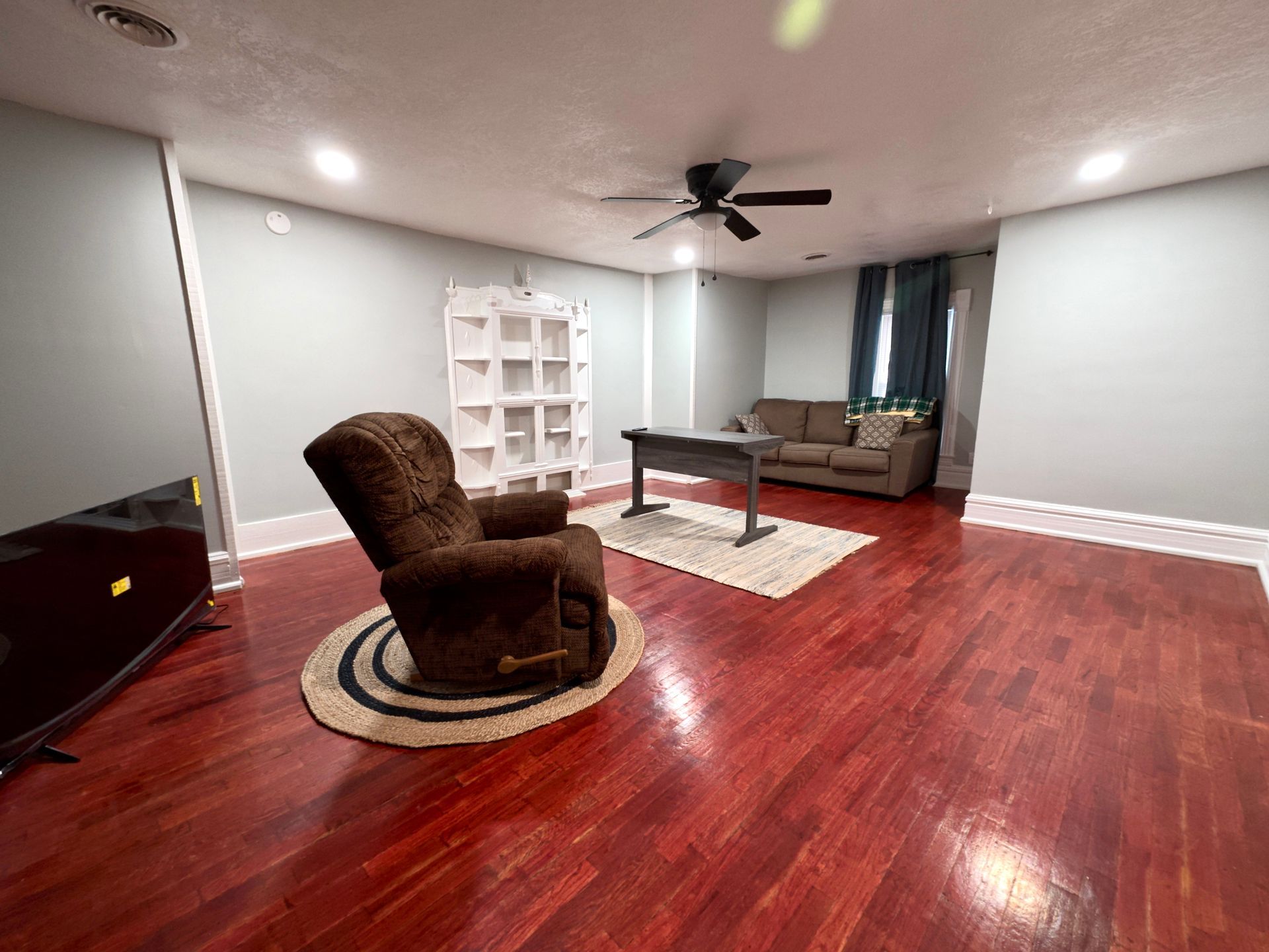 Spacious living room with hardwood floors, a recliner, couch, and shelves.