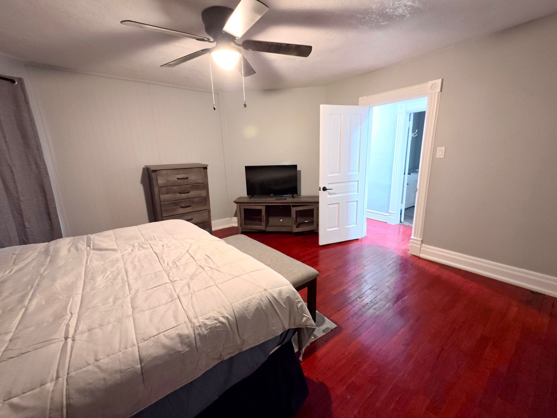 Bedroom with bed, dresser, TV, open doorway, and a ceiling fan; red floor.