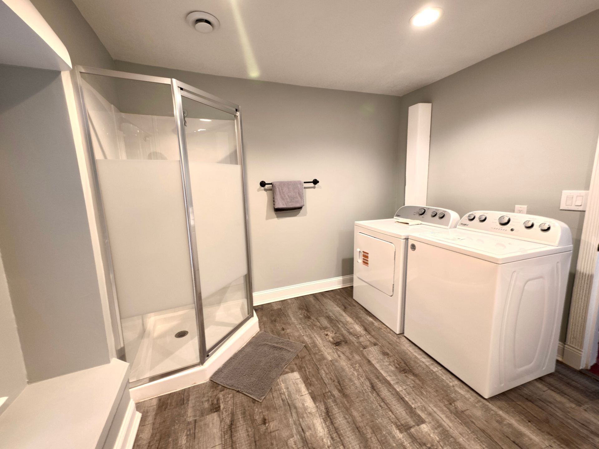 Laundry room with shower, washer, dryer, gray walls, and wood-look flooring.