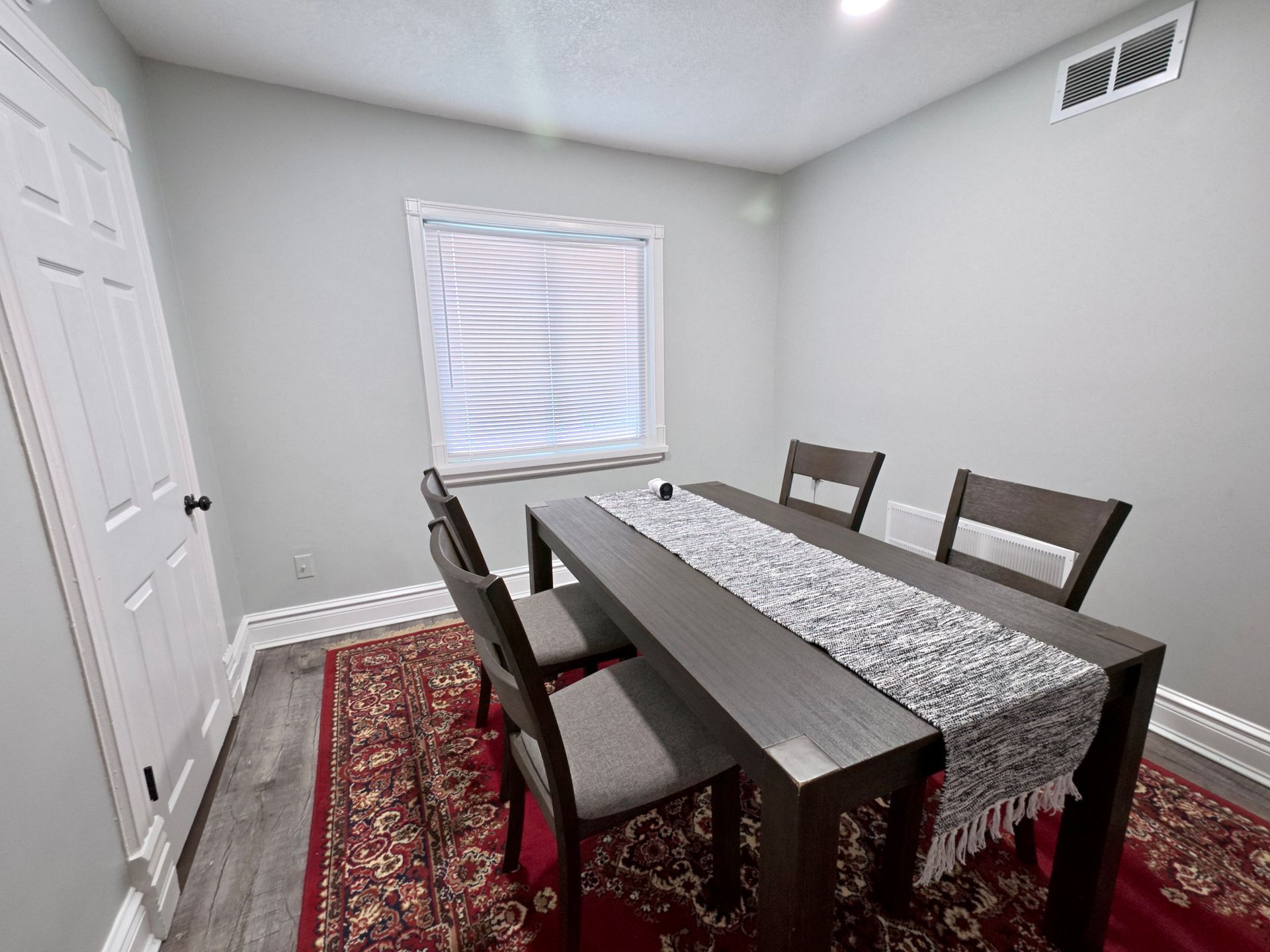Dining room with a table, chairs, rug, window, and door. Gray walls.