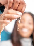 Hands holding house keys, smiling woman in background.