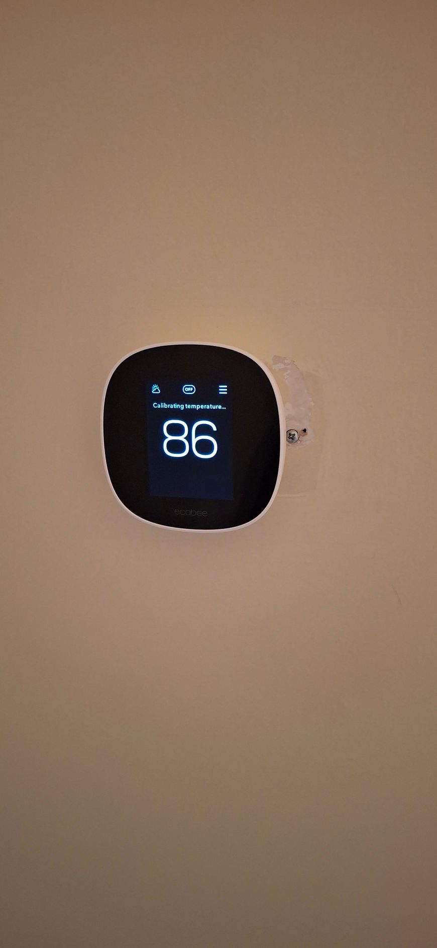 Black smart thermostat displaying the temperature 86 degrees Fahrenheit on a beige wall.
