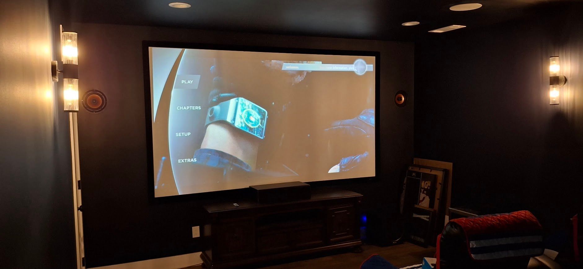 A large screen displays a video game in a dark room with wall sconces.