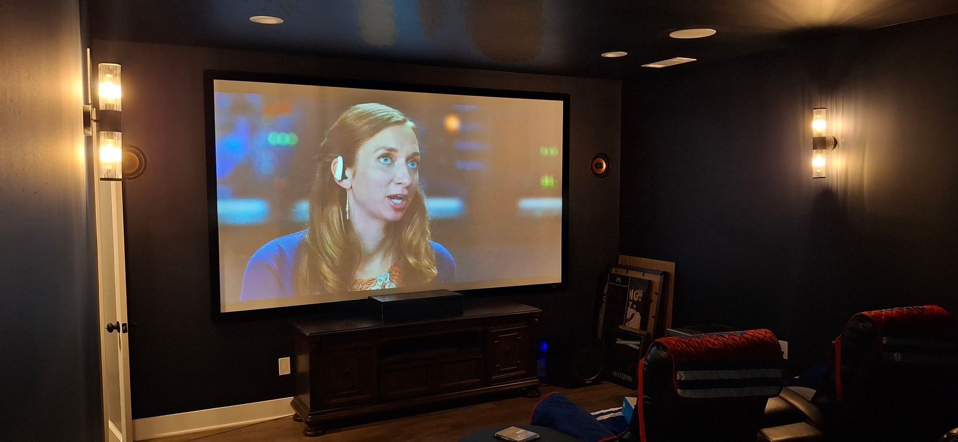 A home theater with a large screen displaying a woman speaking. 
