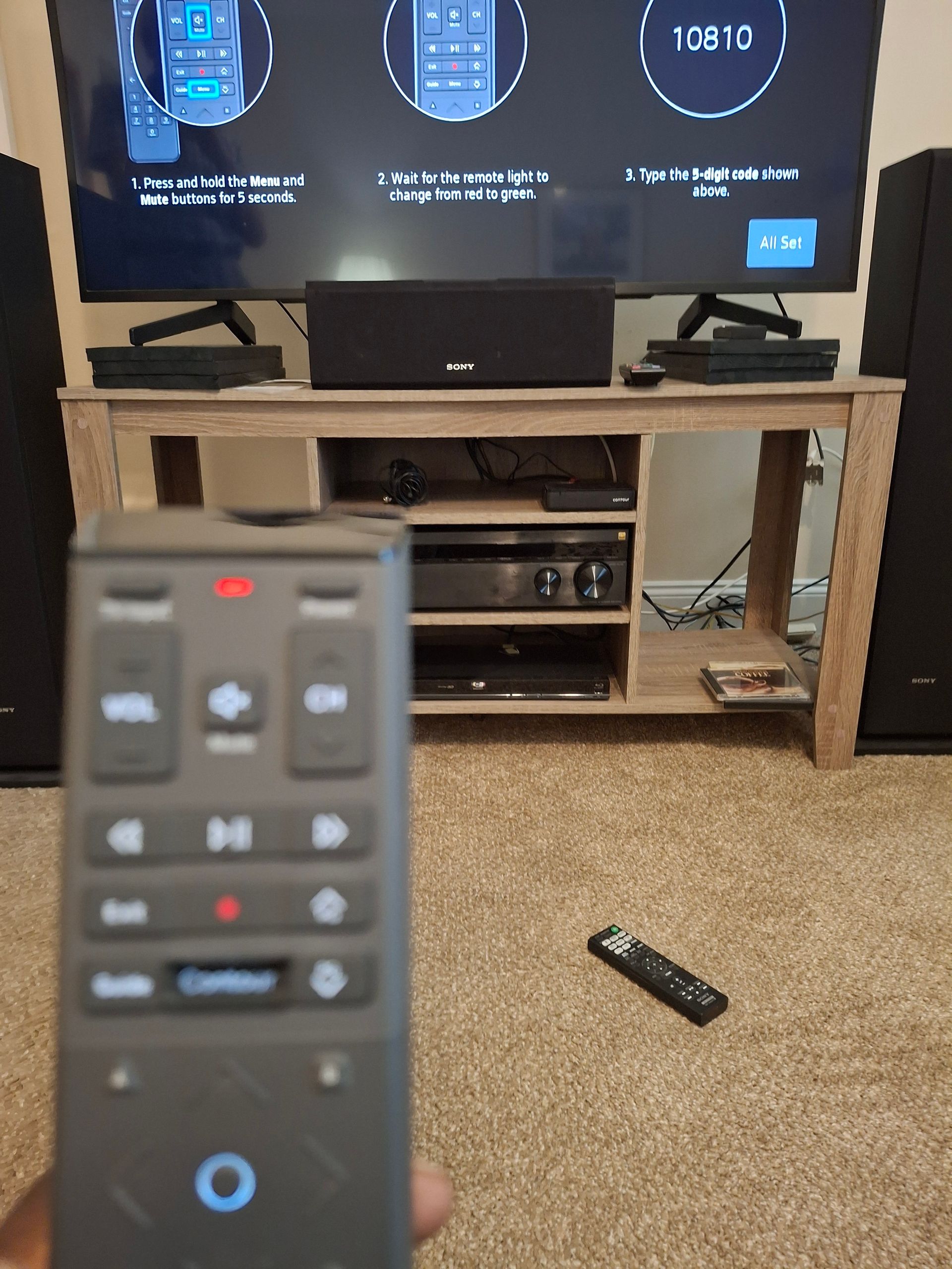 Person holding remote, aiming it toward TV displaying setup instructions. 