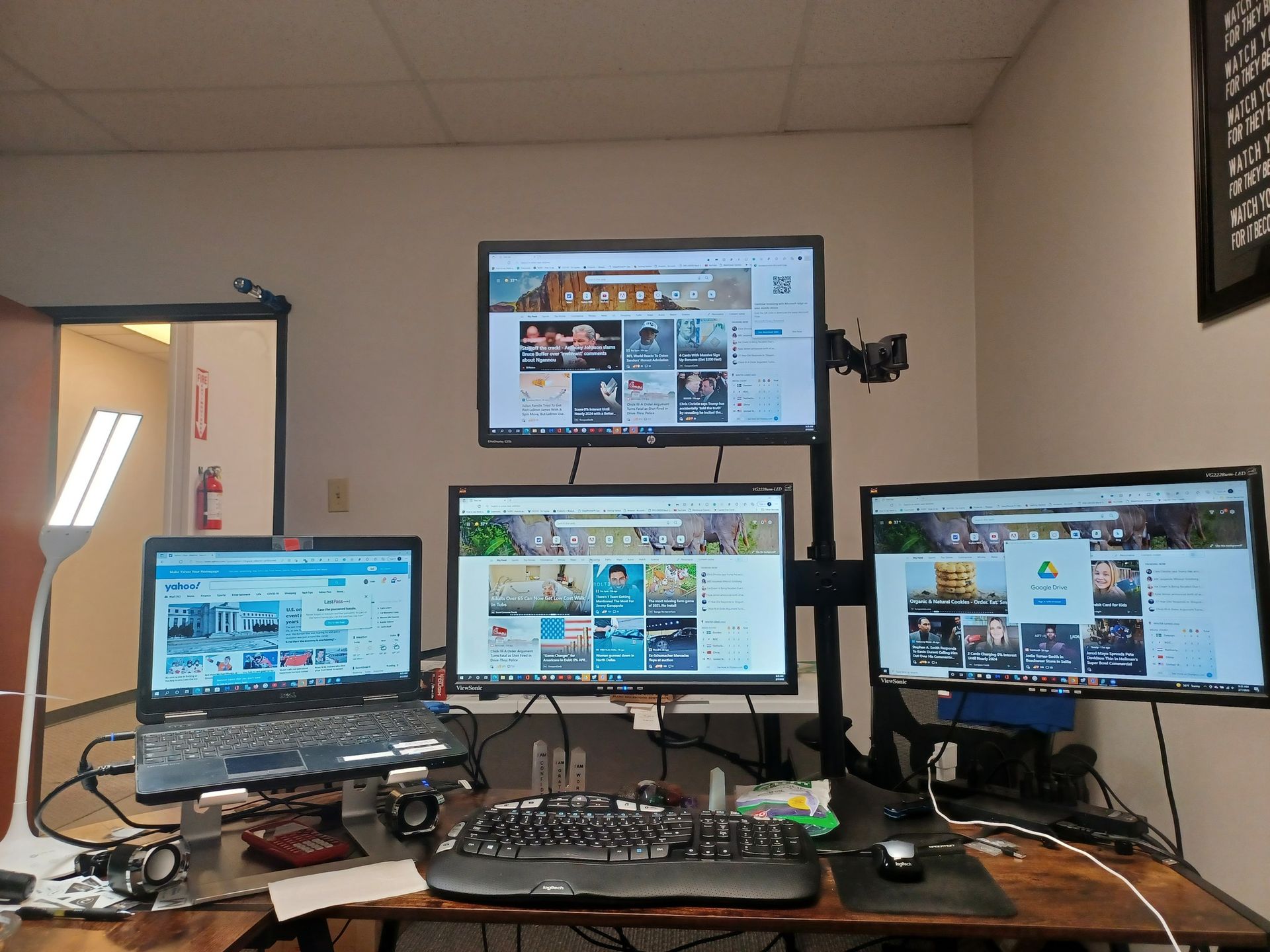 Desk setup with four monitors, a laptop, keyboard, and mouse. Various websites are open on the screens.