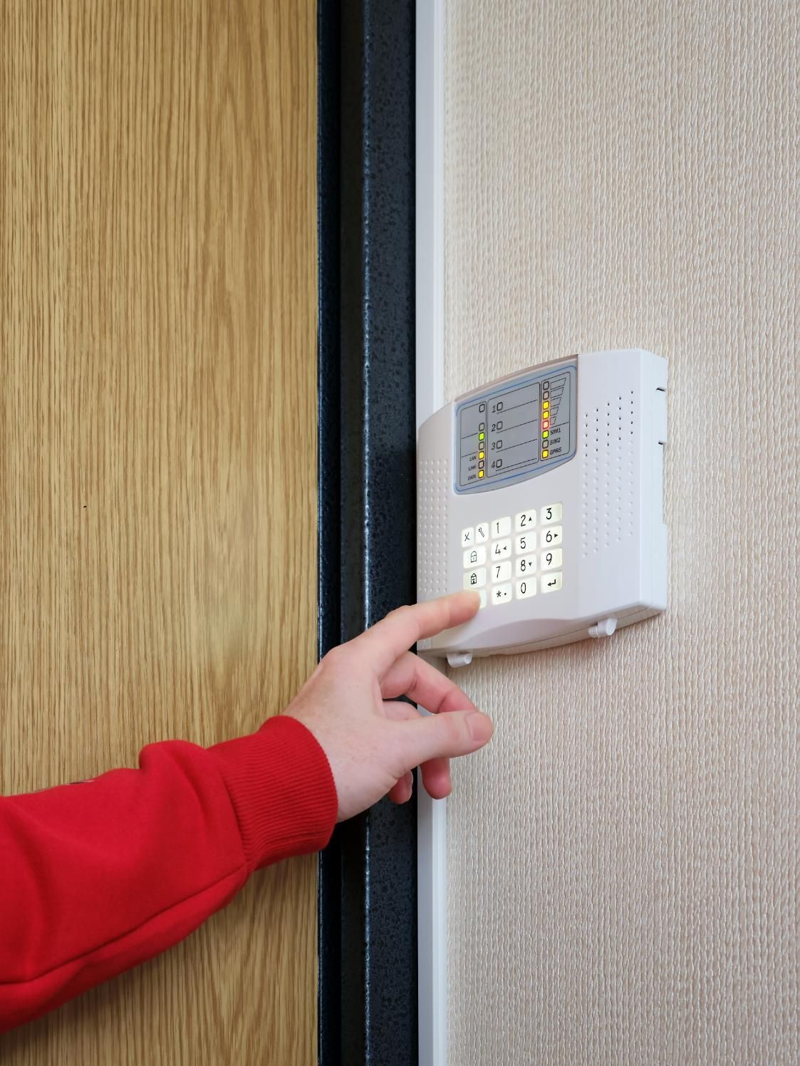 Person entering code on a white security system keypad on a textured wall near a wooden door.