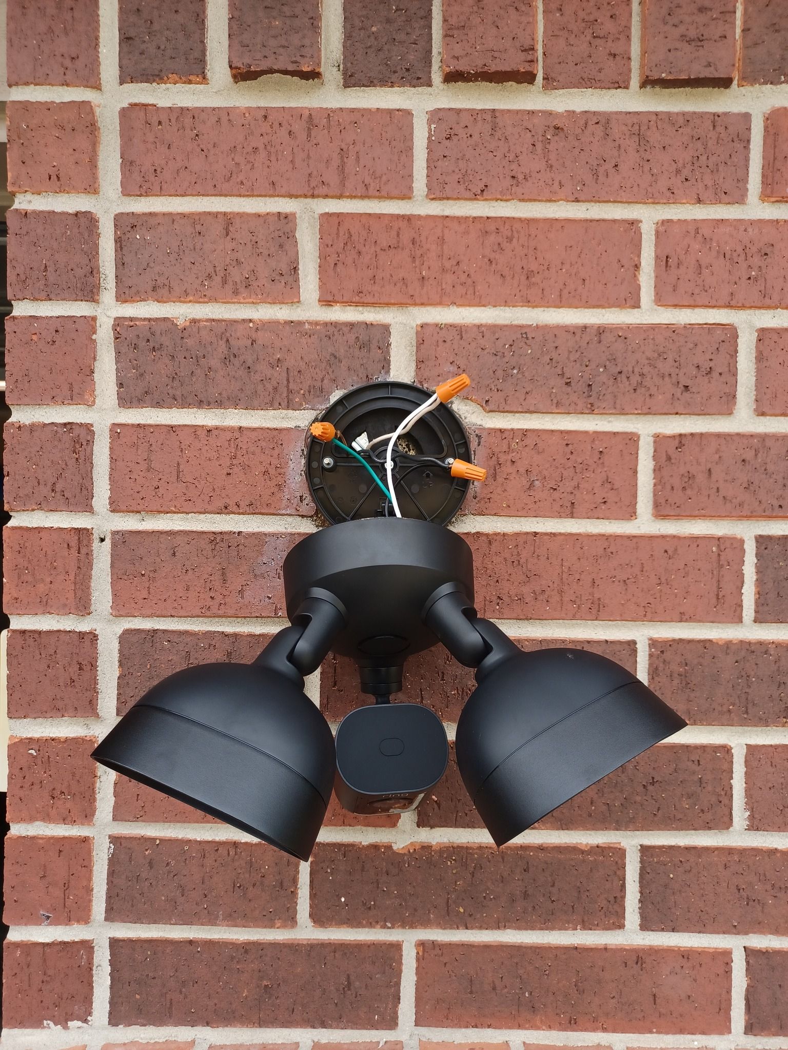 Black floodlight fixture mounted on a red brick wall, with exposed wiring visible.