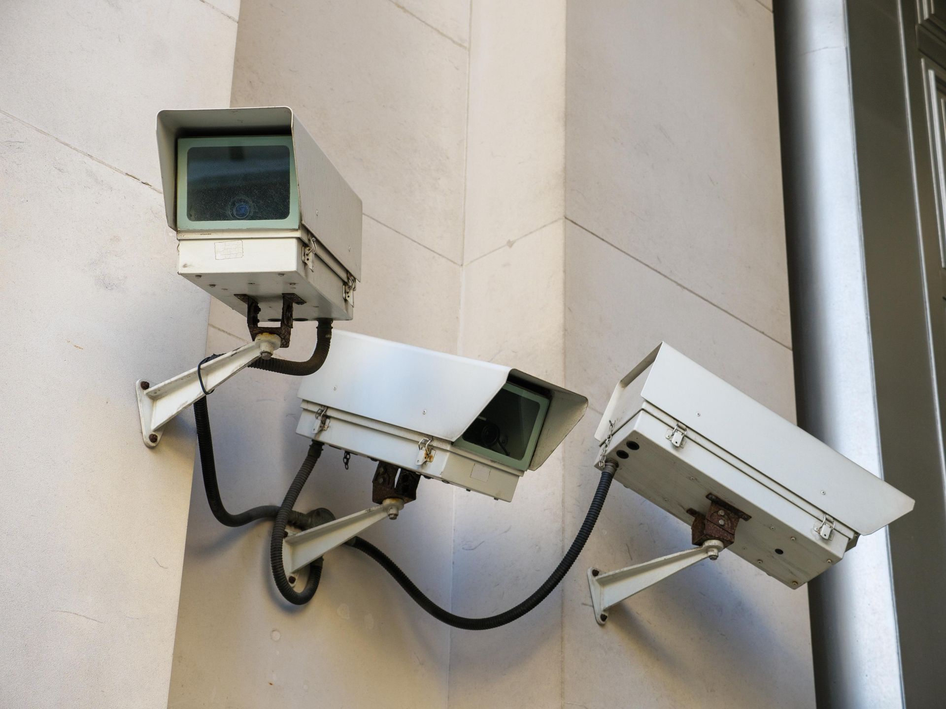 Three white security cameras mounted on a light-colored wall, angled in different directions.