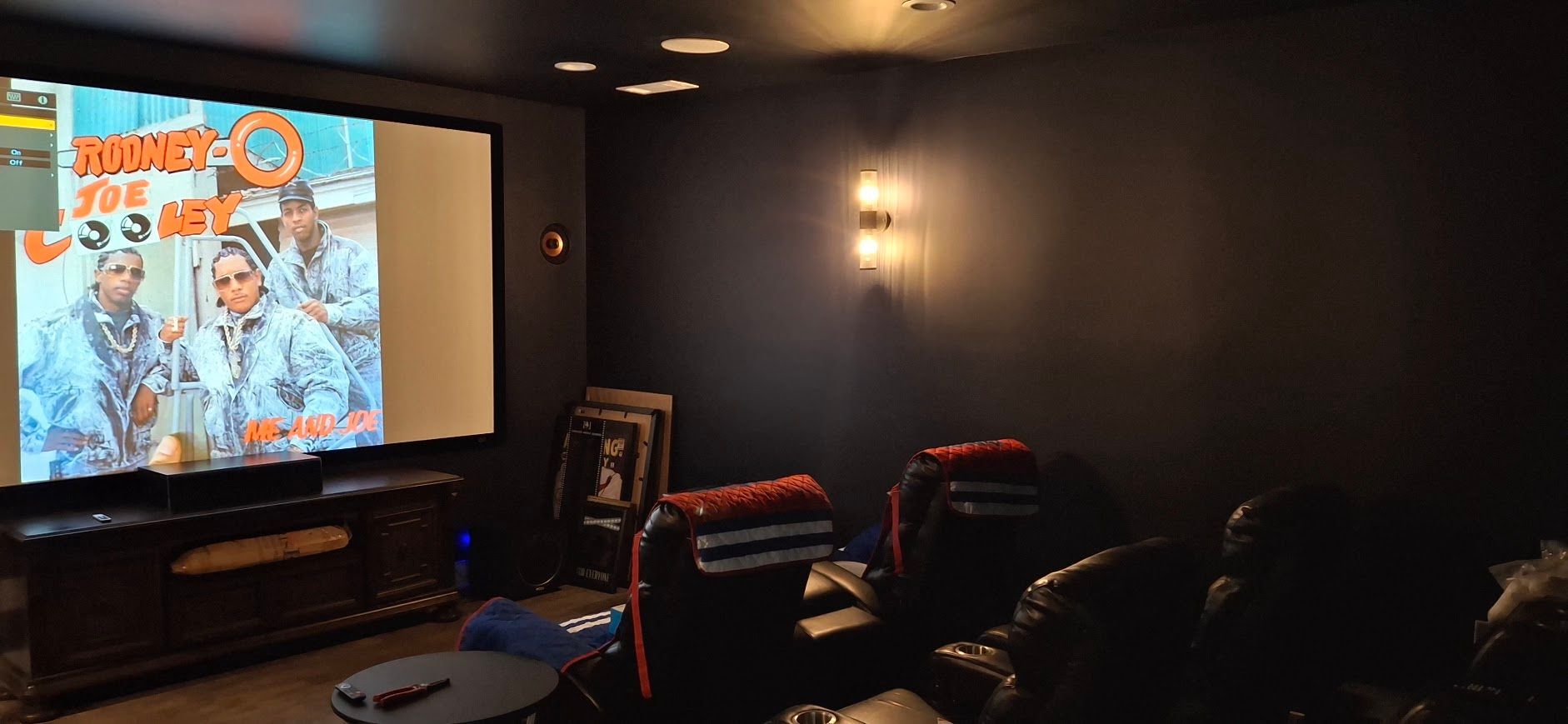 A home theater room with a movie playing on the screen and seating.