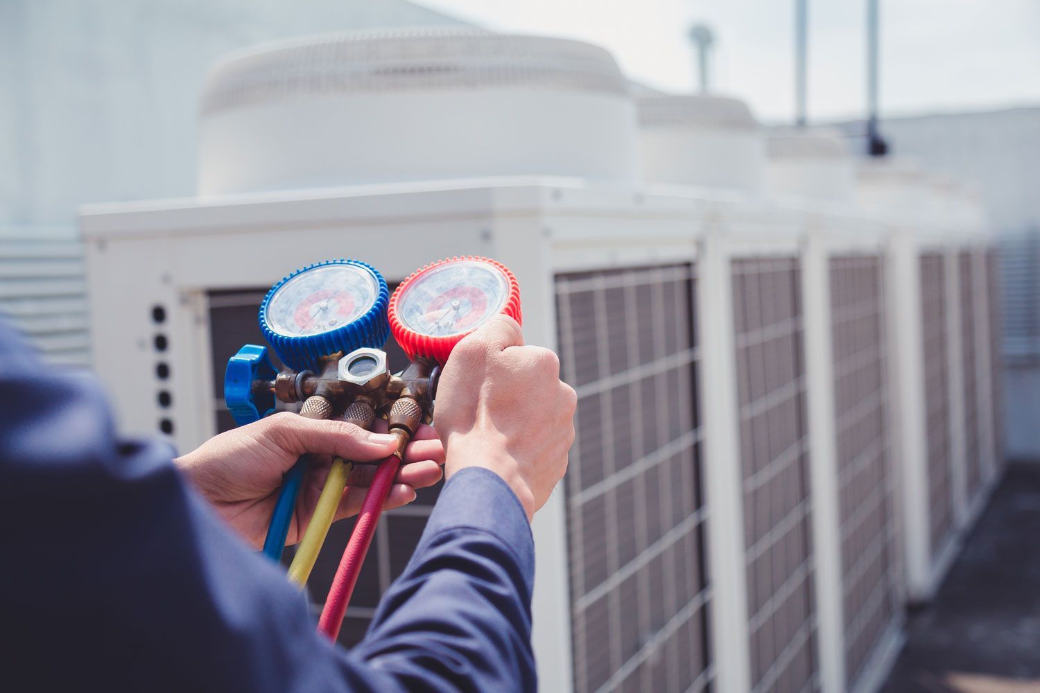 Technician holding HVAC manifold gauges beside rooftop air conditioning units