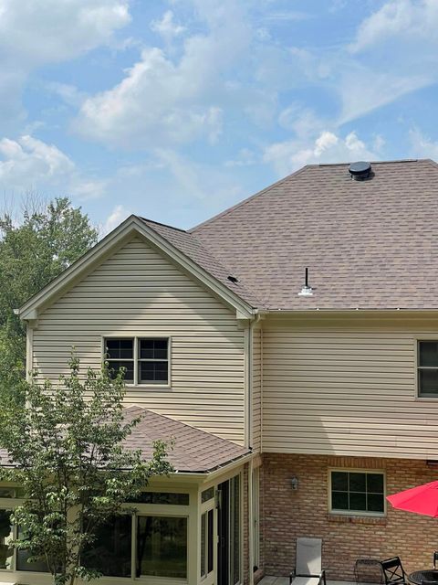 A man is standing on a ladder on the roof of a house.