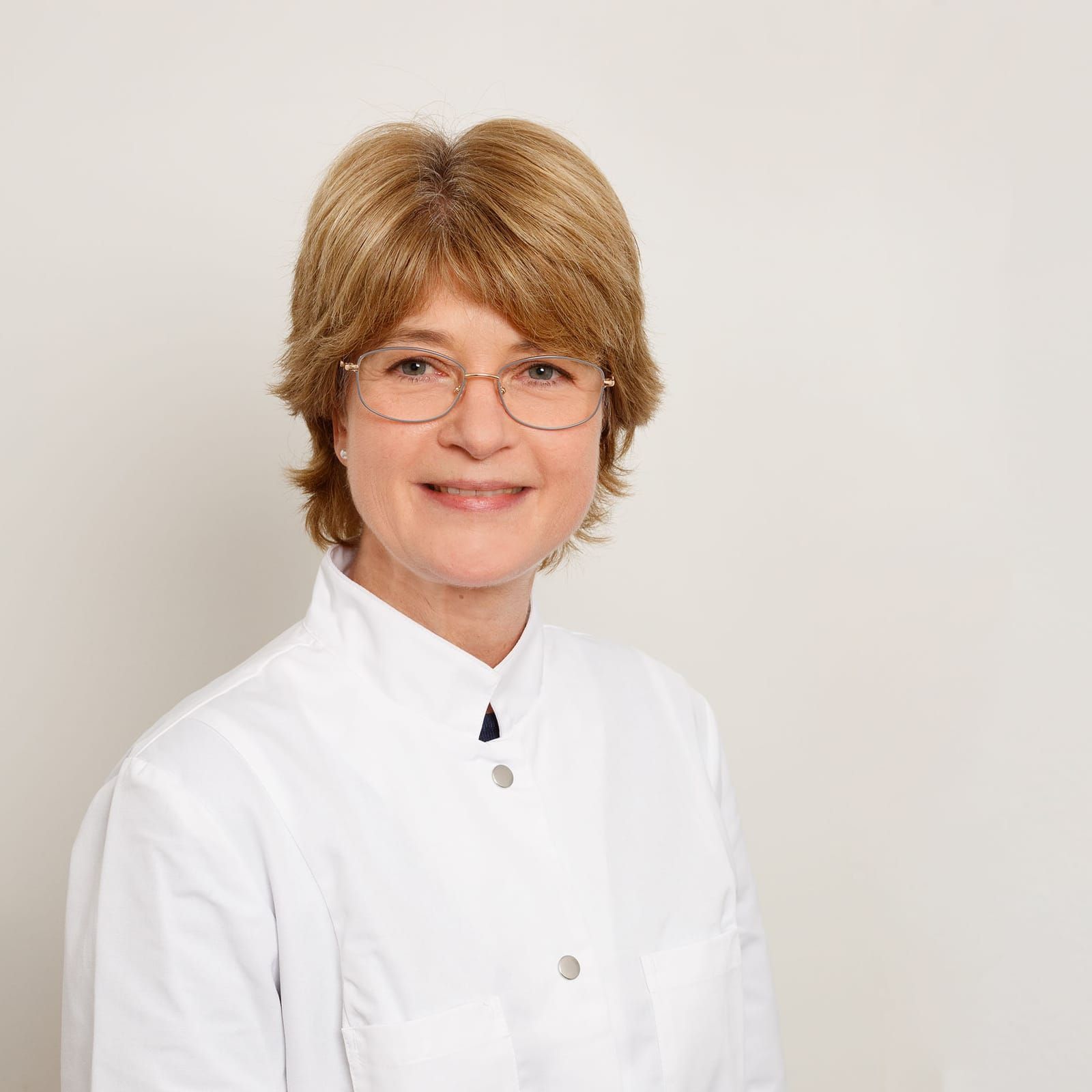 Eine Frau mit Brille und weißem Kittel lächelt in die Kamera.