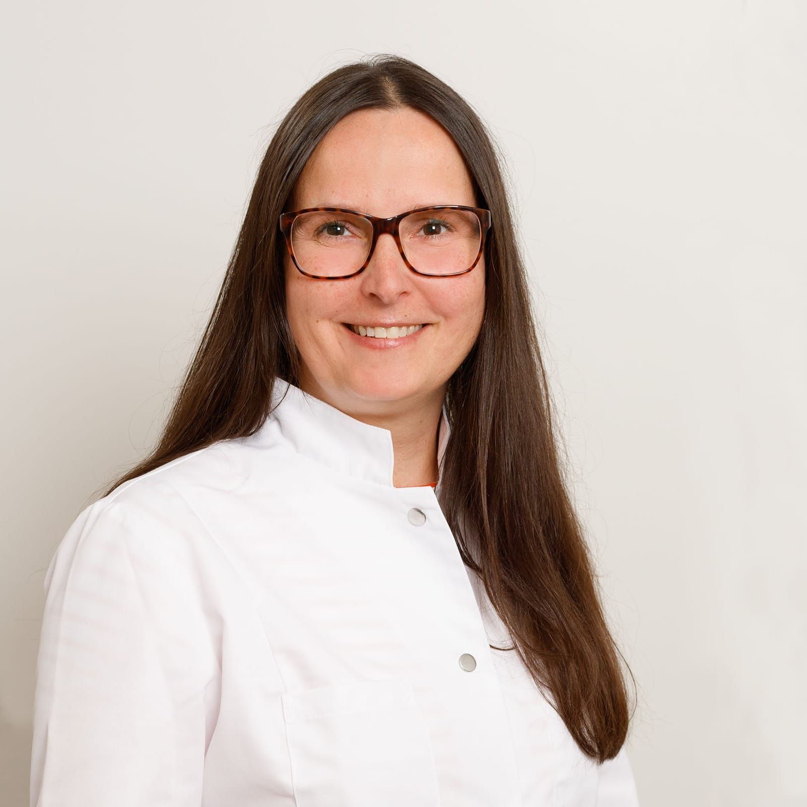 Eine Frau mit Brille und weißem Kittel lächelt in die Kamera.