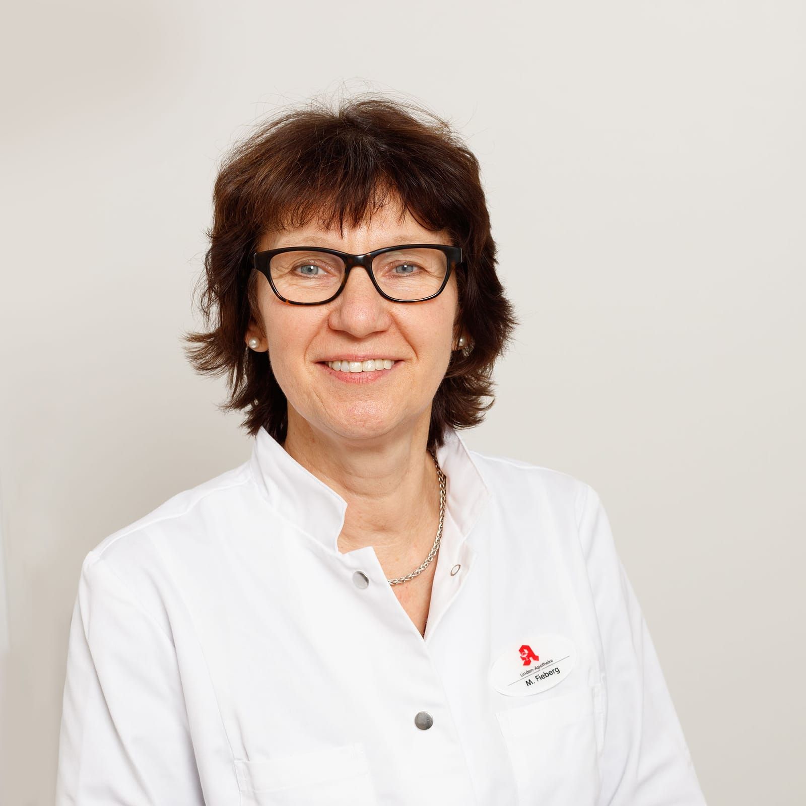 Eine Frau mit Brille und weißem Kittel lächelt in die Kamera.