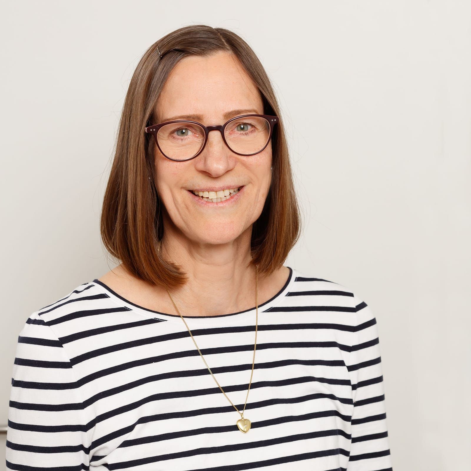 Eine Frau mit Brille und gestreiftem Hemd lächelt in die Kamera.