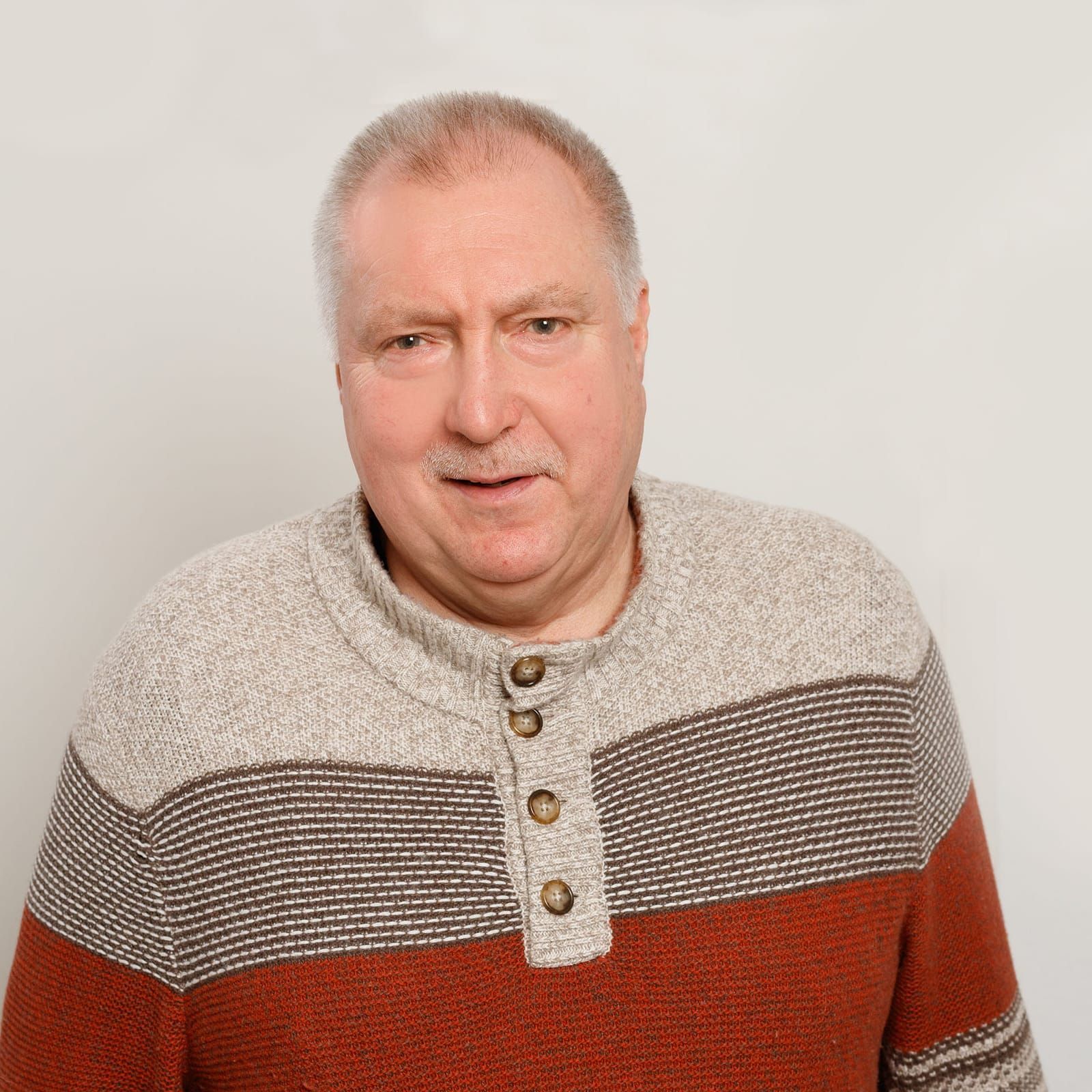 Ein Mann, der einen Pullover mit Knöpfen auf der Vorderseite trägt, steht vor einer weißen Wand.