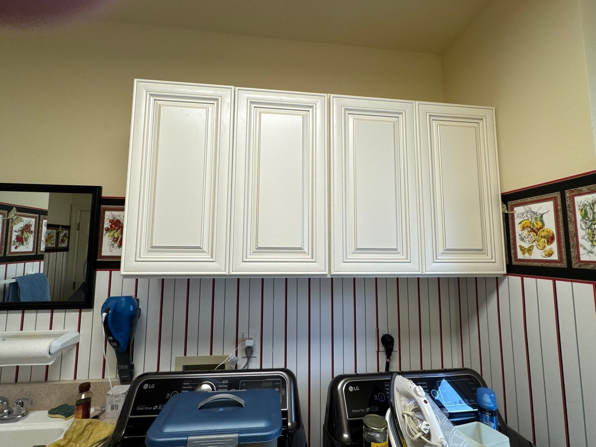 White cabinets above washing machines. Striped wall, mirror, and decorations.