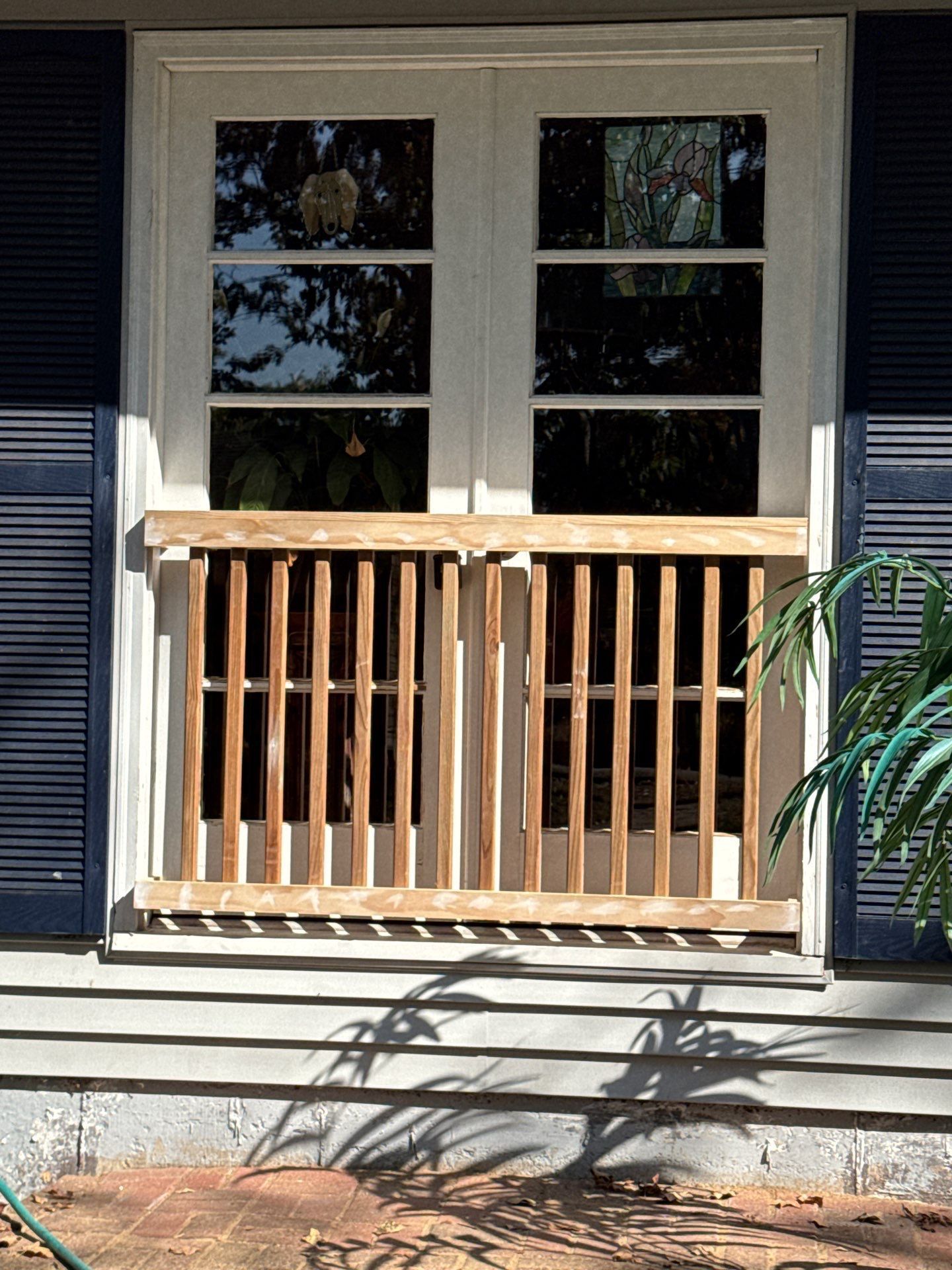 Wooden bars installed on a window for security. Blue shutters and a white frame are visible.