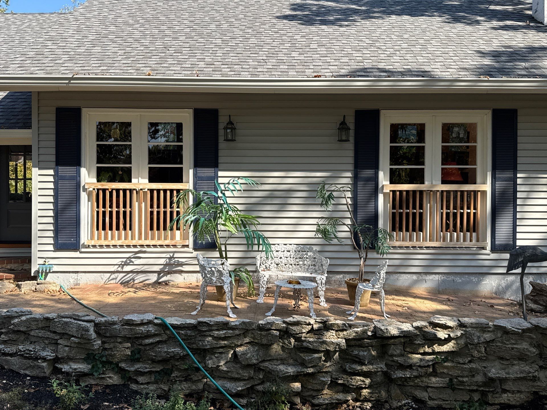 Exterior of a house with two windows, a small seating area, and a stone retaining wall.