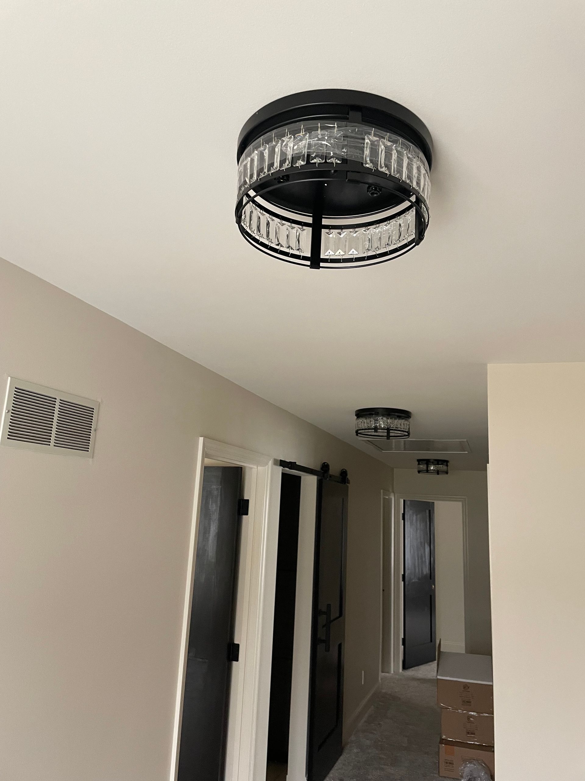 A hallway with a crystal ceiling light and dark barn doors.