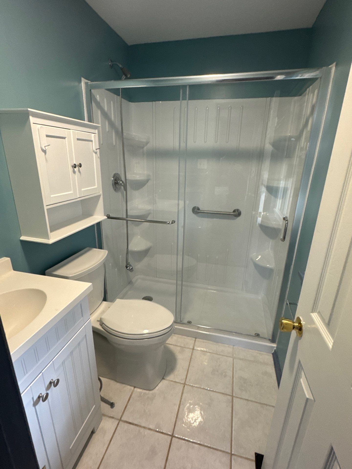 Bathroom with white fixtures: toilet, vanity, medicine cabinet, shower with grab bars; teal walls, tile floor.
