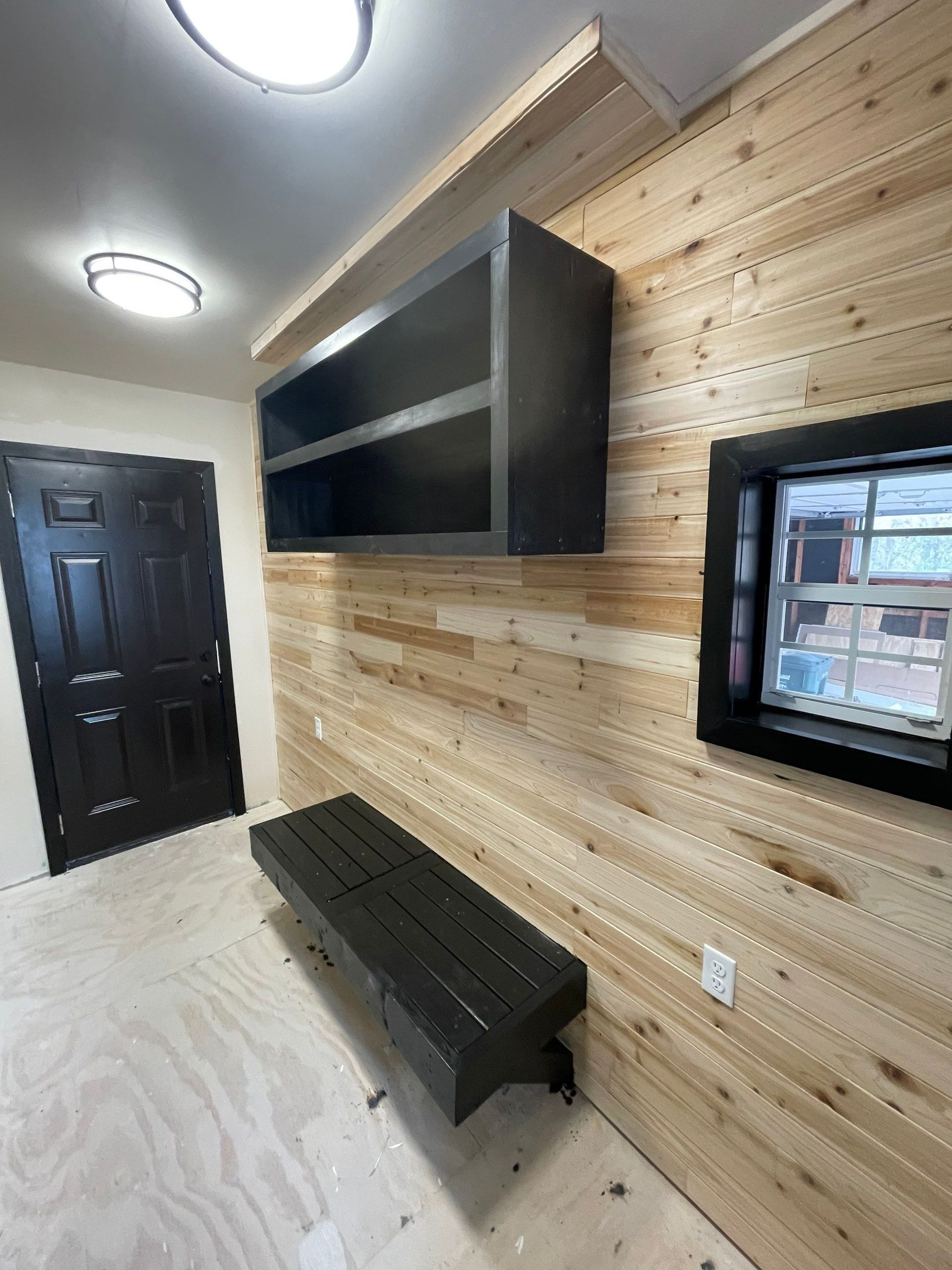 Interior view with wooden paneling, black shelving, bench, door, and window.