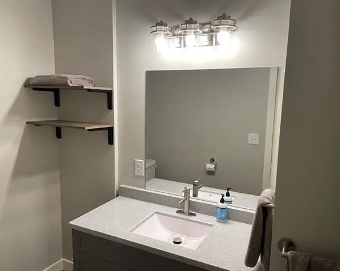 Bathroom with sink, mirror, floating shelves holding towels, and light fixture.