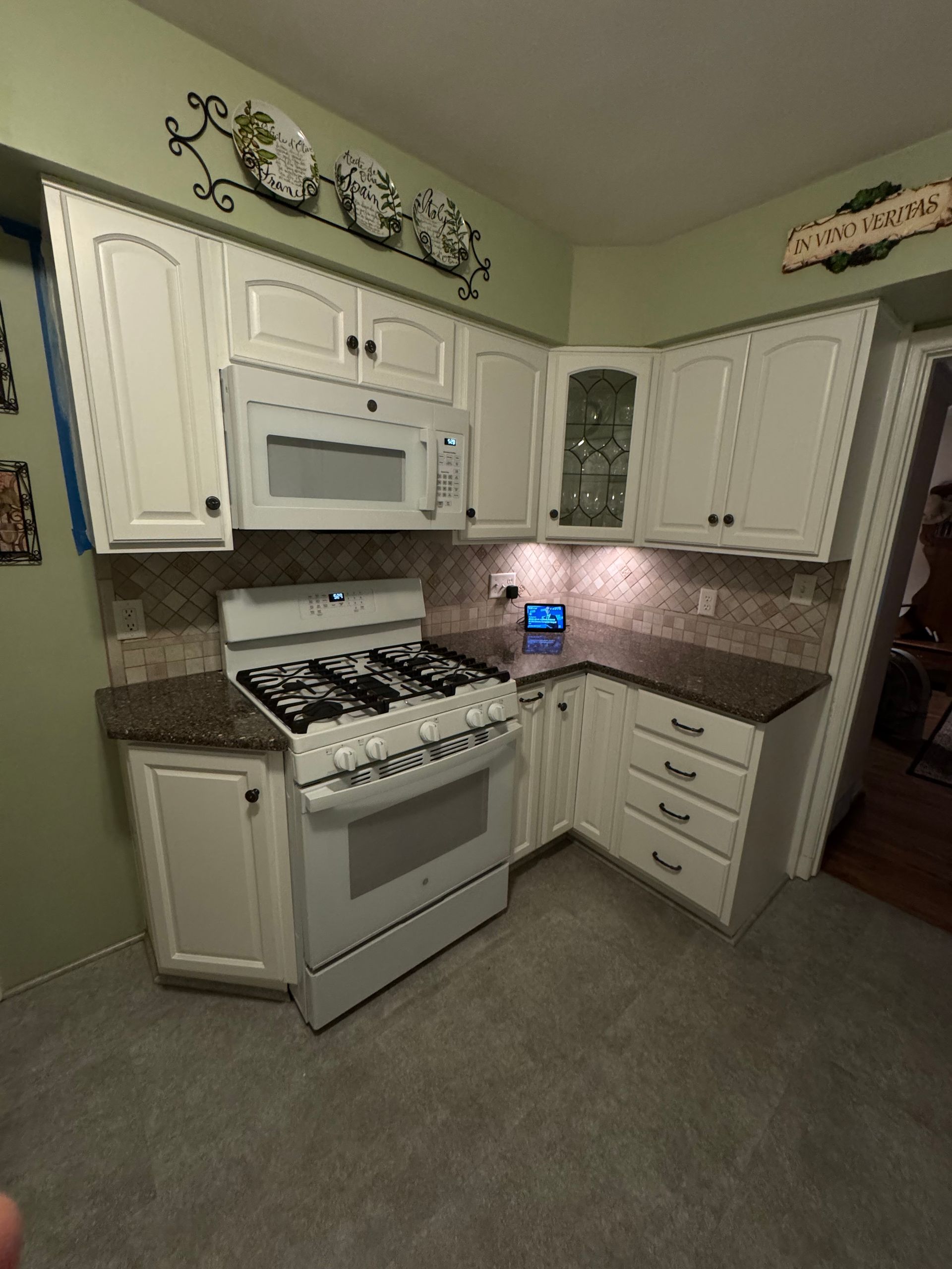 White kitchen cabinets, stove, and microwave. Dark countertops and backsplash. Grey flooring.