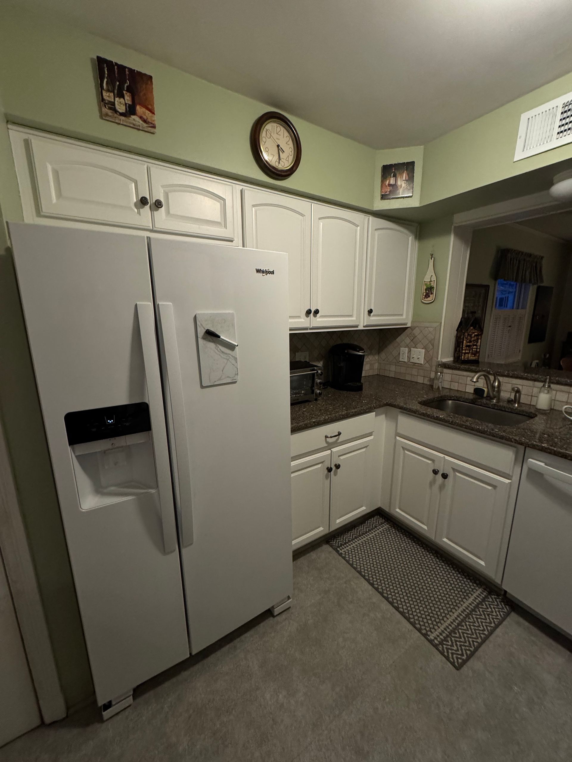 White kitchen with refrigerator, cabinets, countertop, rug, and appliances.