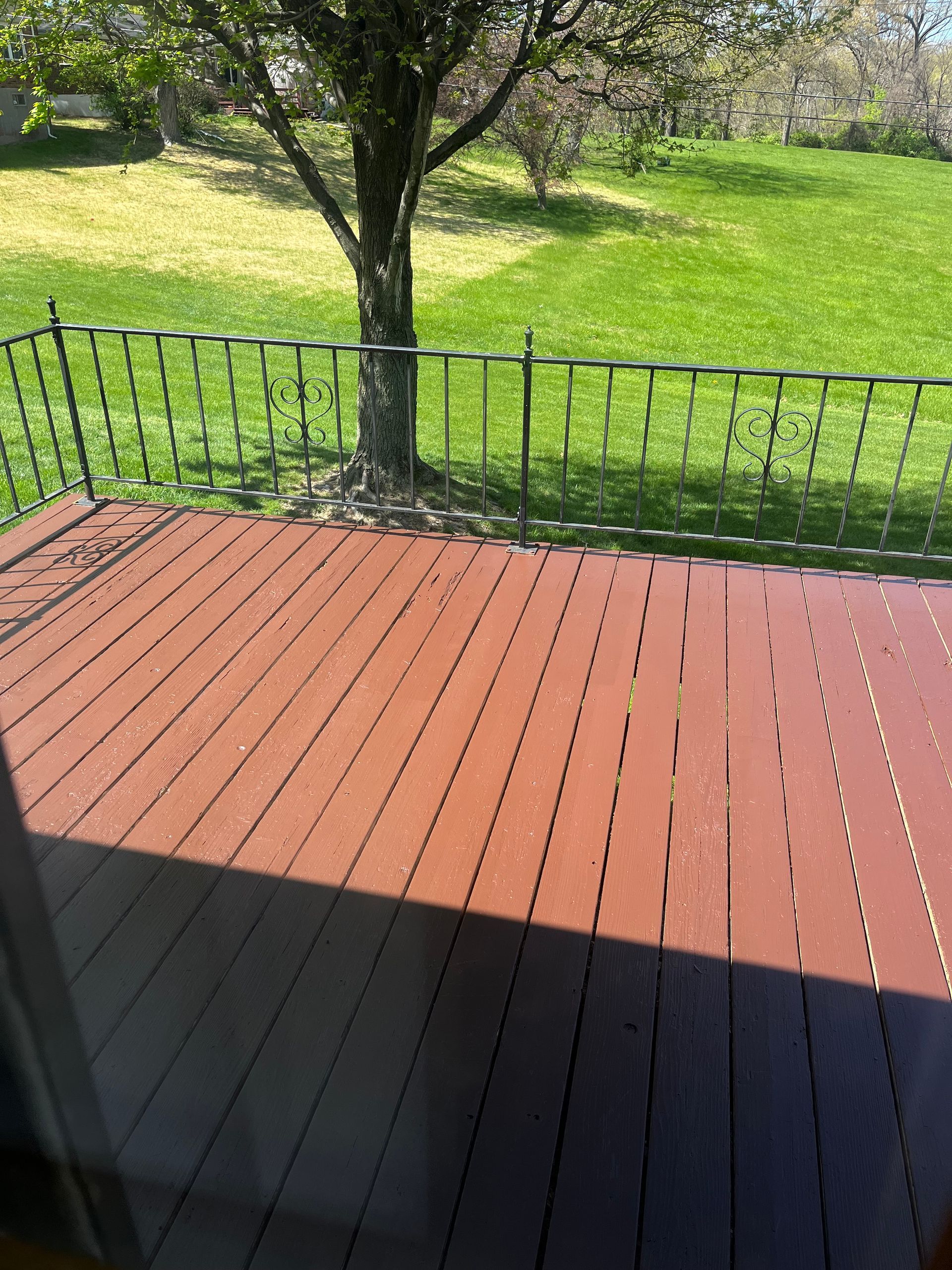 Wooden deck with metal railing overlooking a grassy yard and a tree.