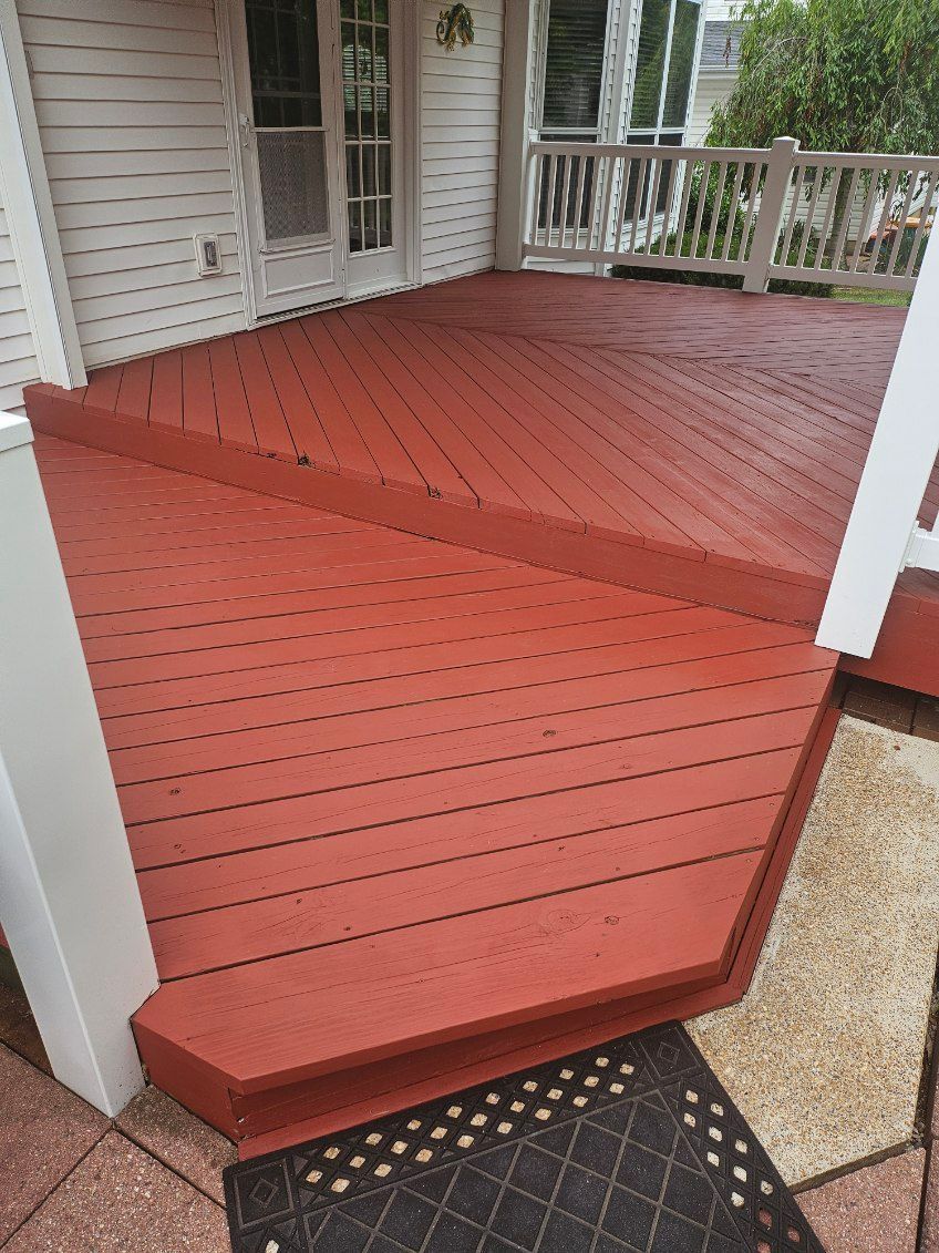 Red painted wooden deck with angular design, next to a white house.