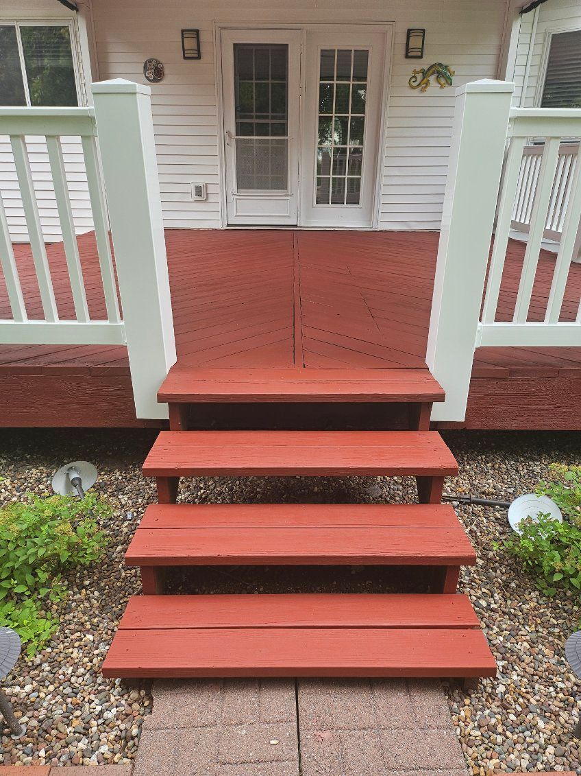 Red wooden steps leading to white double doors, with a red bench and white railing on a deck.