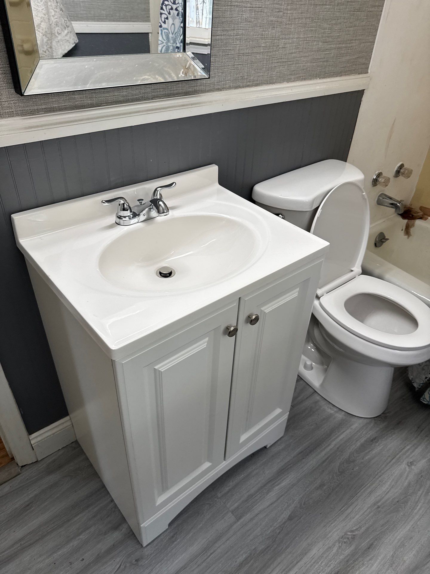 White bathroom vanity with sink and two doors; toilet to the right. Gray walls and floor.
