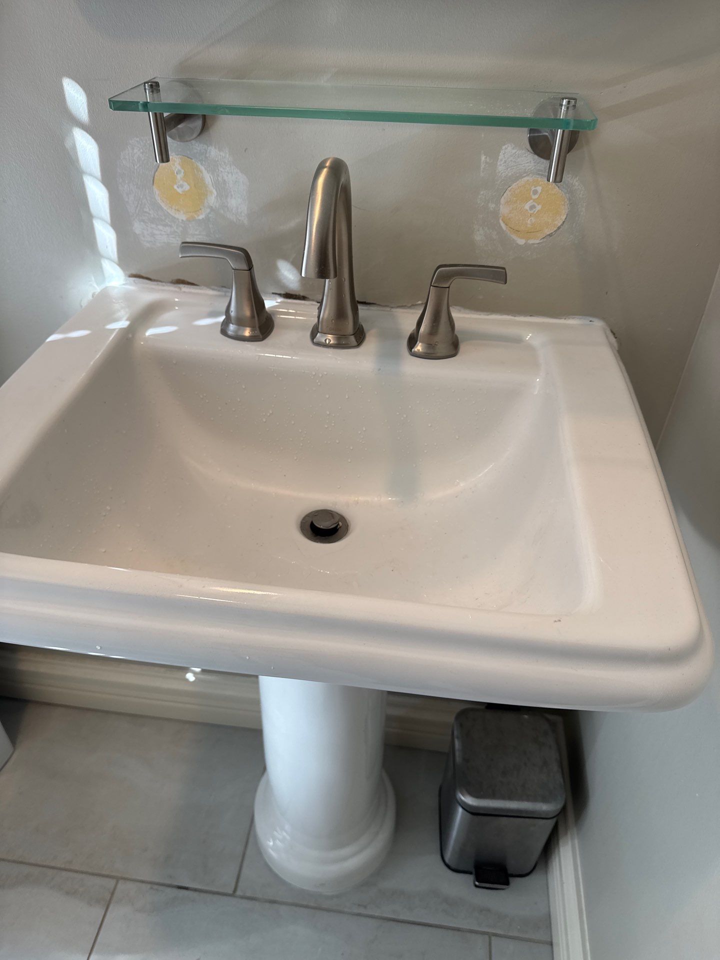 White pedestal sink with chrome faucet and handles, a glass shelf above.