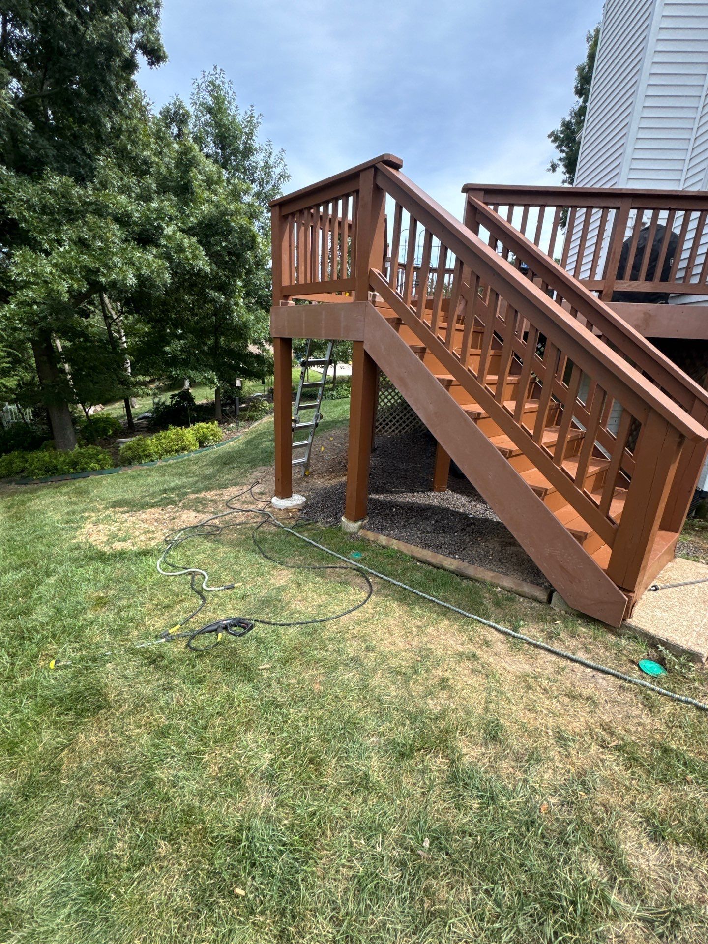 Wooden deck with stairs, brown stain. Green grass surrounds it. Blue sky overhead.